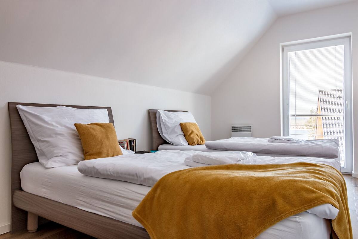 A modern bedroom with two beds, white bedding, and a large window with blinds.
