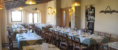 A restaurant with multiple tables set for dining, wooden chairs, and pendant lighting.