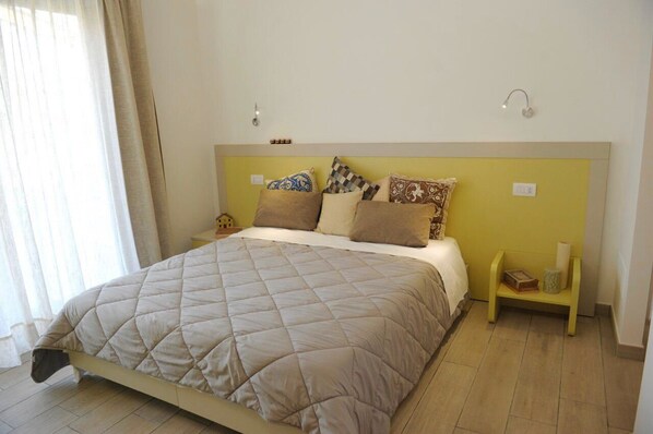 Een slaapkamer met een bed, kussens, nachtkastjes en een raam met gordijnen.