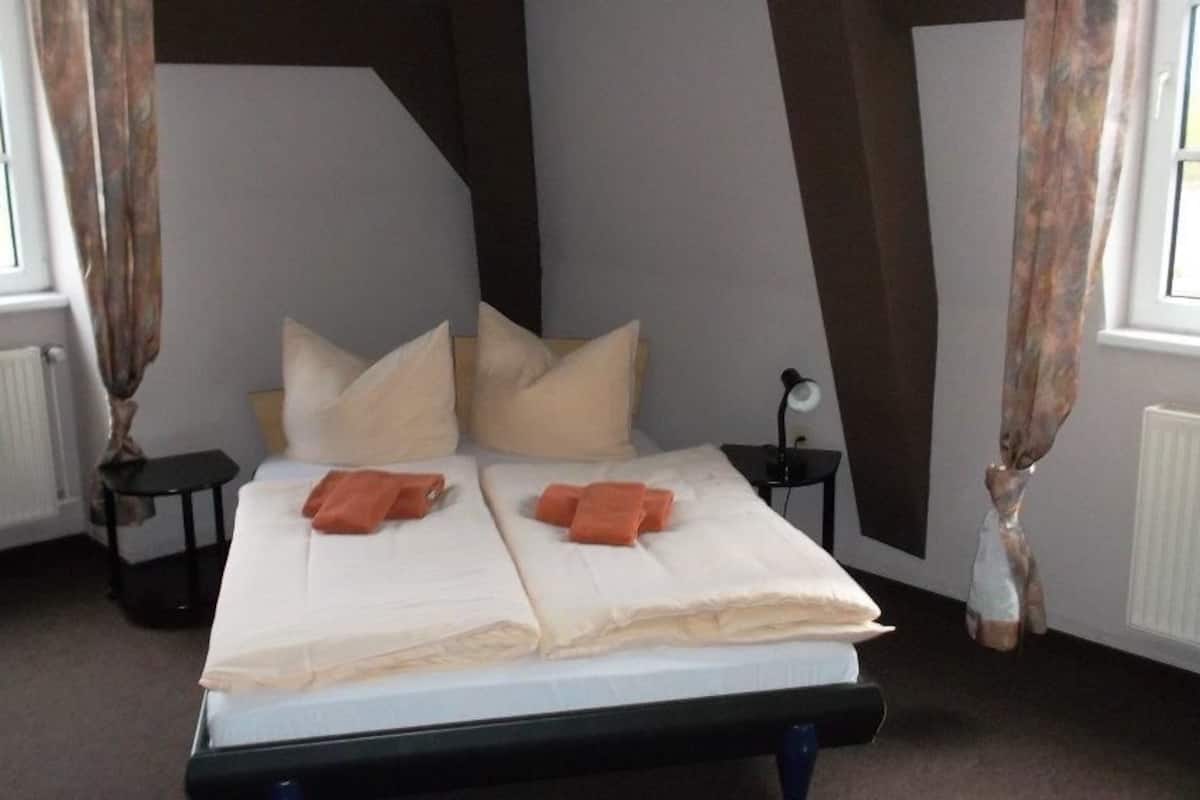 A bedroom with a bed, pillows, a nightstand, a lamp, and curtains.