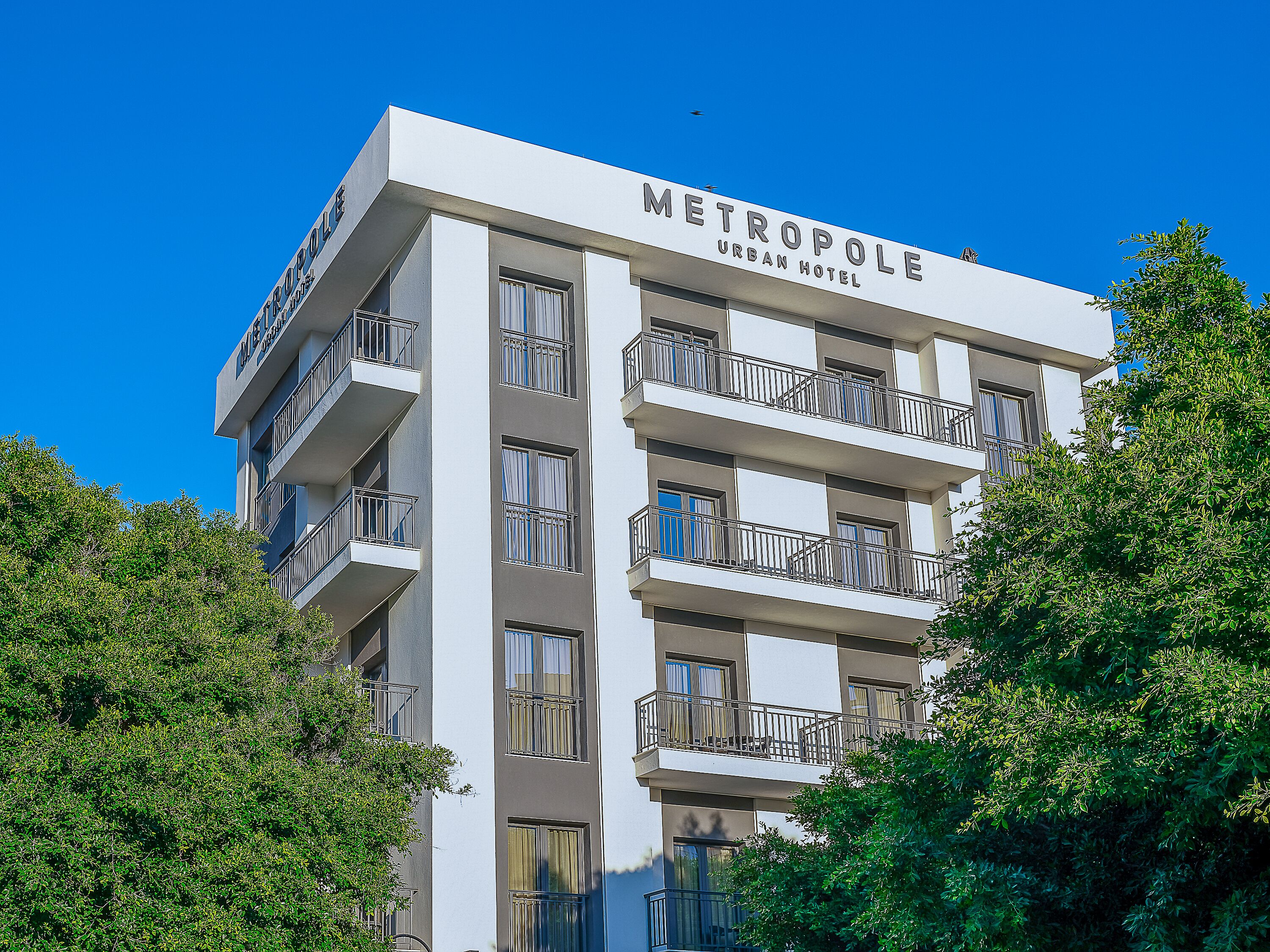 Un hotel de varios pisos llamado METROPOLIS URBAN HOTEL, con balcones y ventanas.