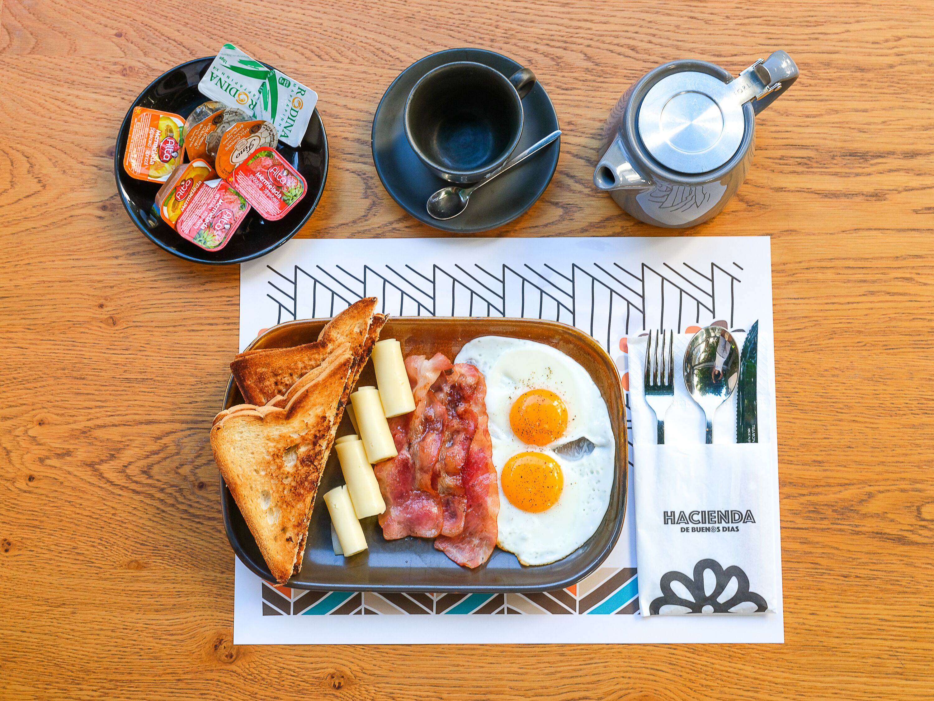 Un plateau de petit-déjeuner avec des toasts, des œufs et du bacon, posé sur une table en bois.