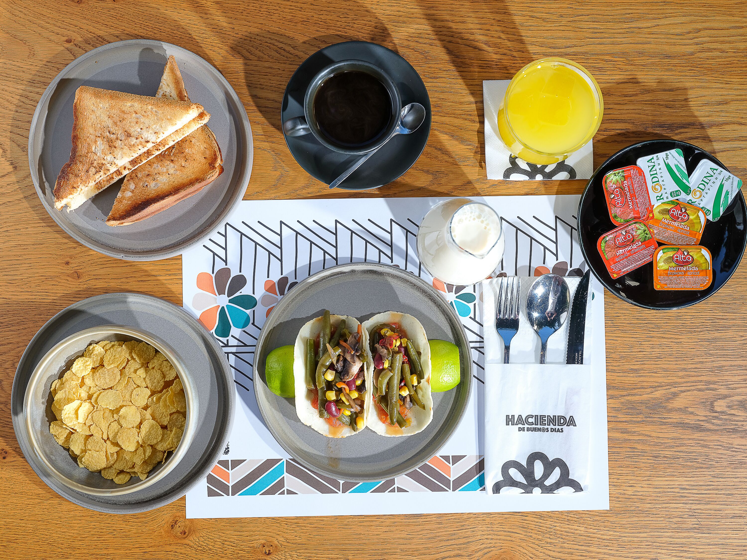 A breakfast table with toast, coffee, juice, a bowl of chips, a plate of tacos, and a plate of yogurt.
