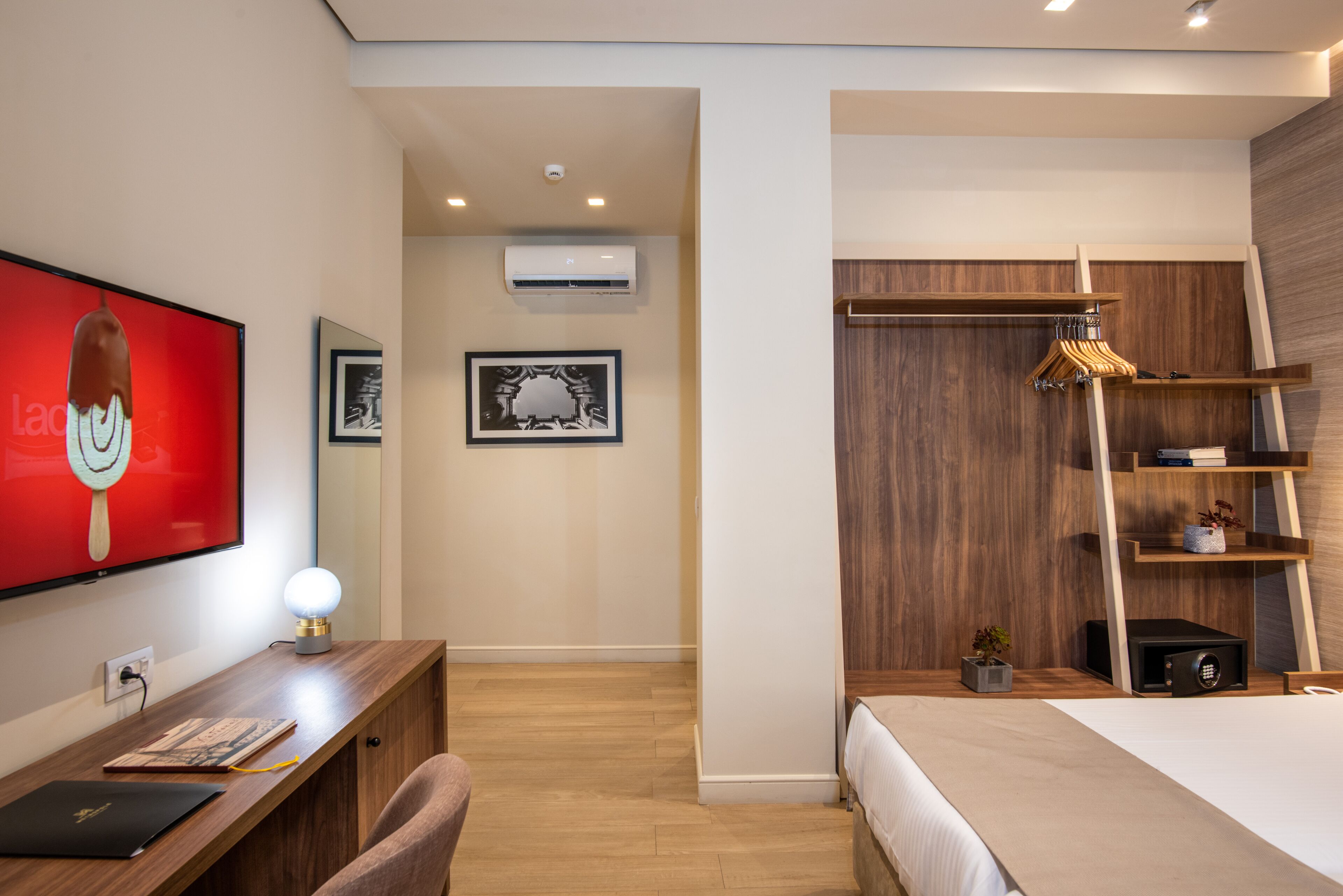 Een moderne slaapkamer met een houten bureau, een bed, een kledingkast en een televisie waarop een dessert wordt weergegeven.
