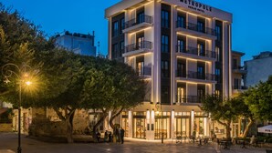 Un hotel urbano moderno con varios balcones, una entrada bien iluminada y mesas al aire libre.