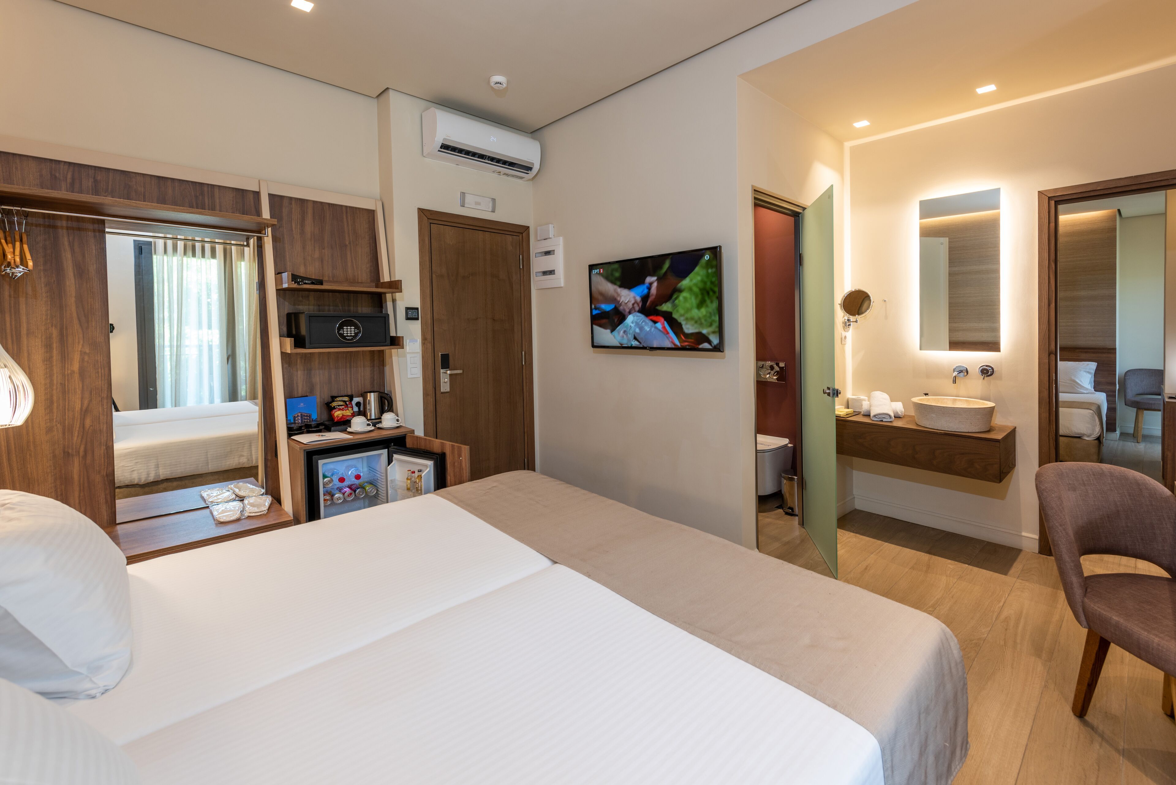 A hotel room with a bed, a TV, a desk with a computer, a microwave, a mini-fridge, a vanity with a mirror, and a chair.