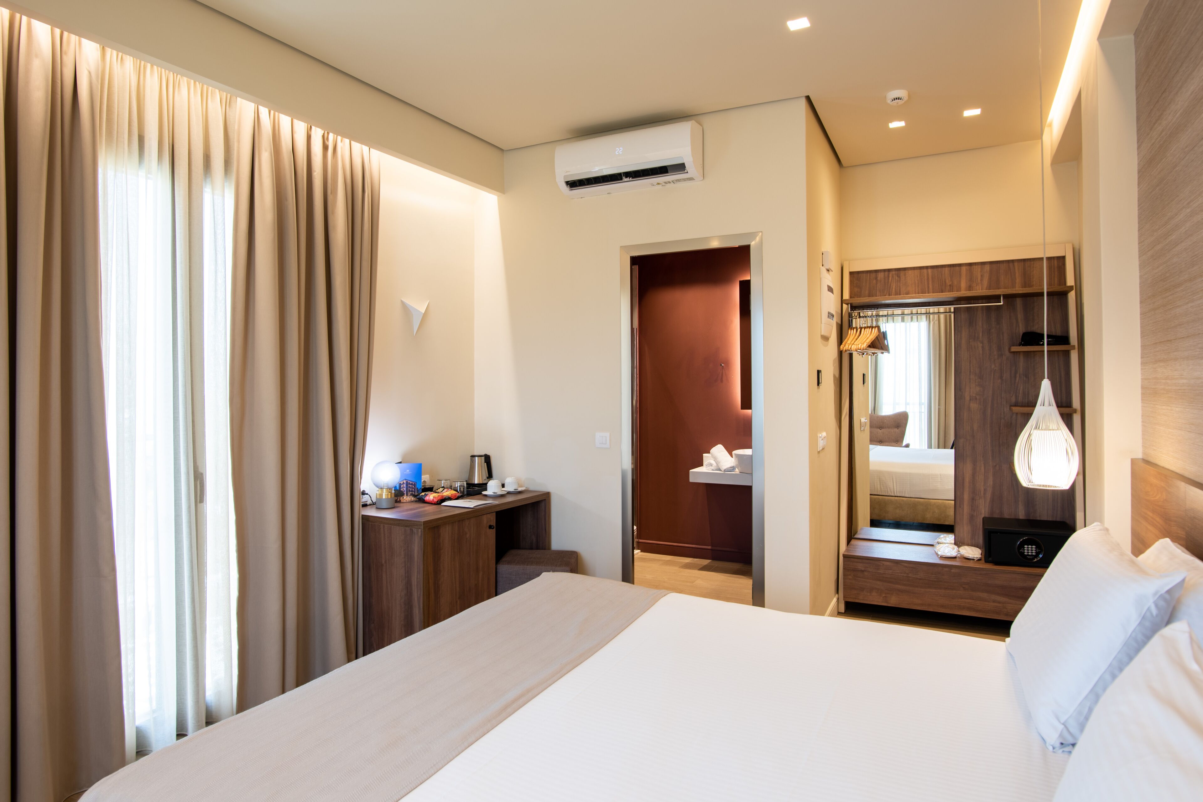 Hotelkamer met een groot bed, een bureau met lamp, een airconditioning en een spiegel met hanglamp.