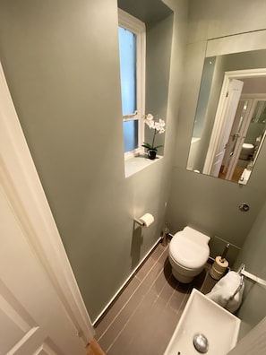 A small bathroom with a toilet, sink, and window. - Apartment Next to Victoria Station (London)