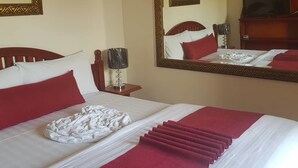 Ein ordentlich bezogenes Bett mit roter und weißer Bettwäsche, ein Spiegel mit dekorativem Rahmen sowie ein Fernseher an der Wand.