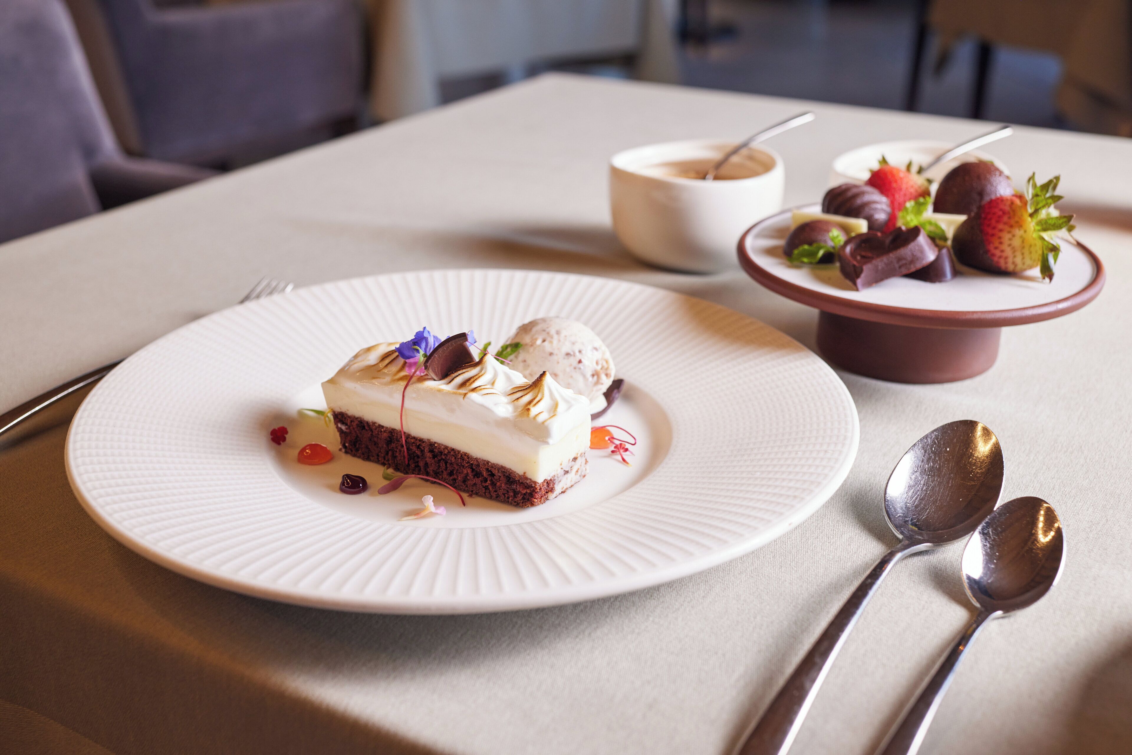 A dessert plate with a slice of cake and ice cream, a bowl of soup, and a plate with strawberries and chocolate on a table.