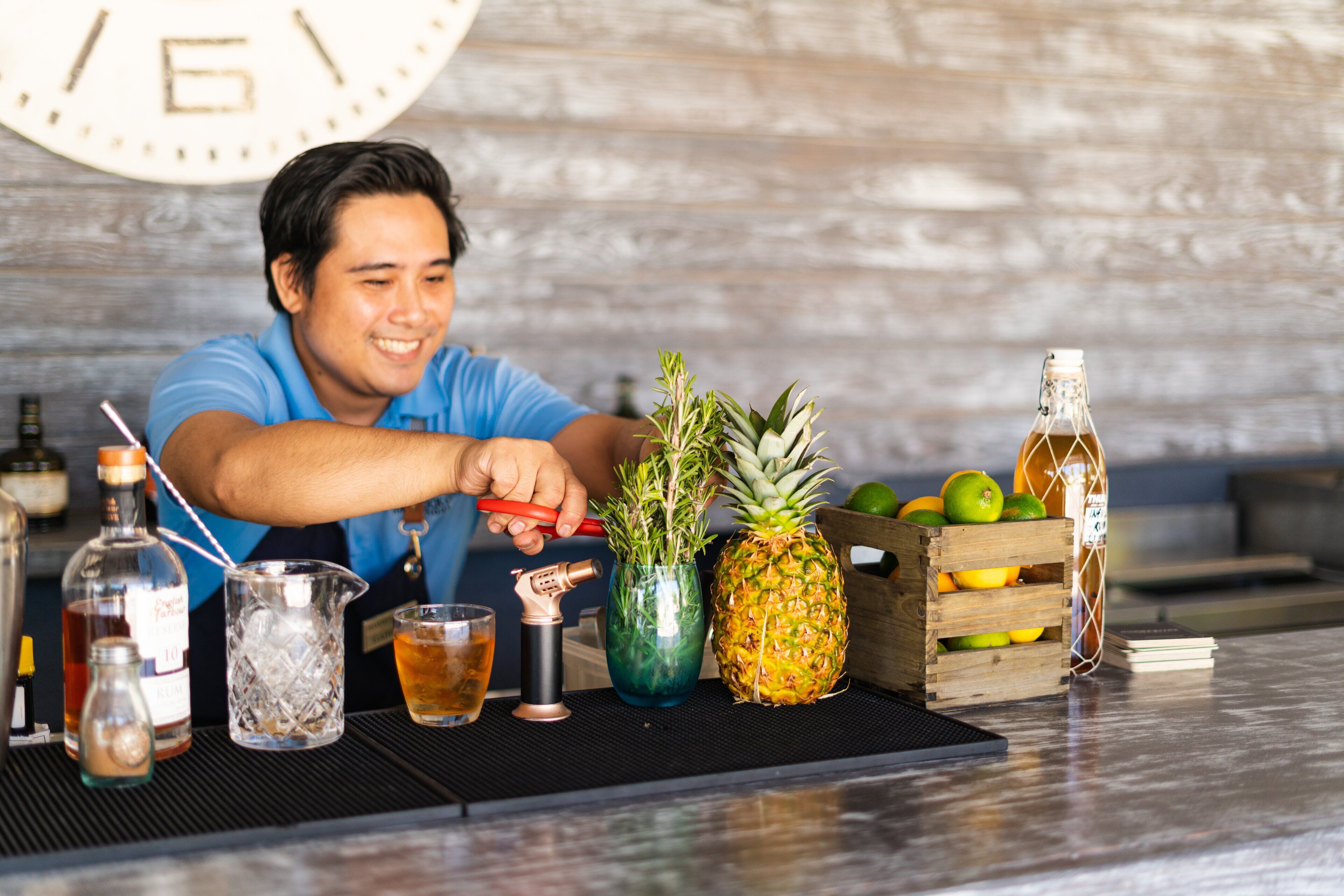 Ein Barkeeper bereitet einen Cocktail mit verschiedenen Flaschen und einer Ananas auf der Theke zu.