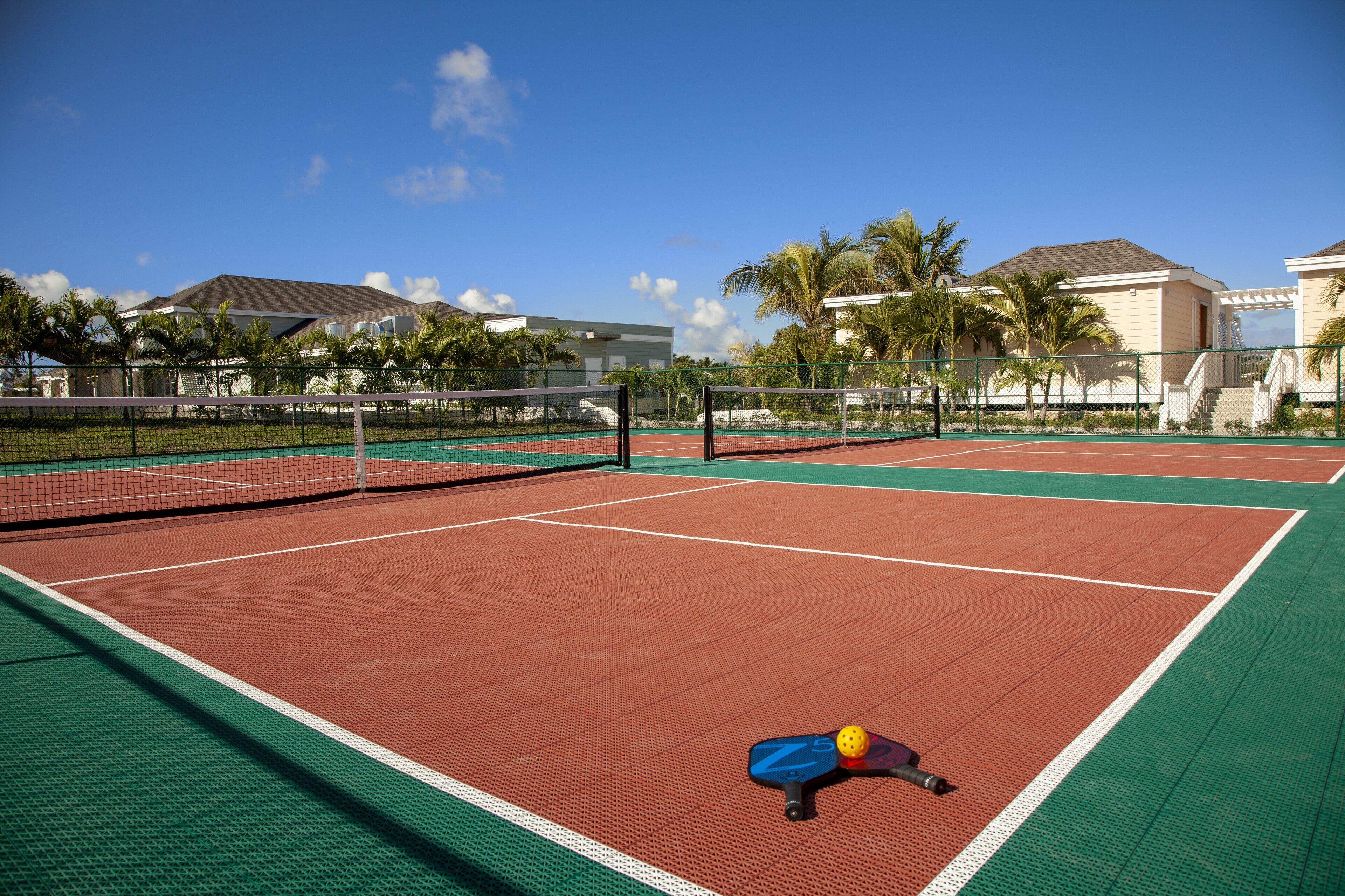 A tennis court with a net, surrounded by a fence and palm trees.