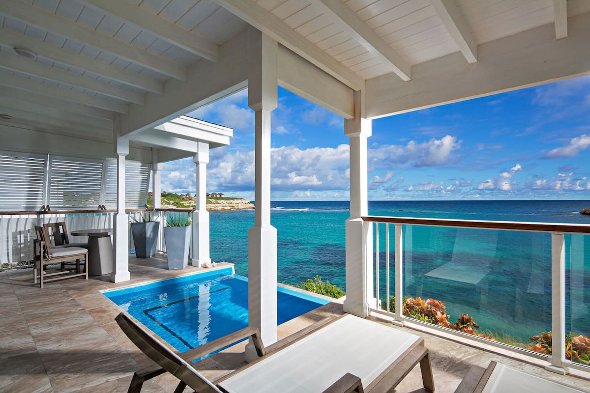 A covered outdoor area with a pool, lounge chairs, and a view of the ocean.