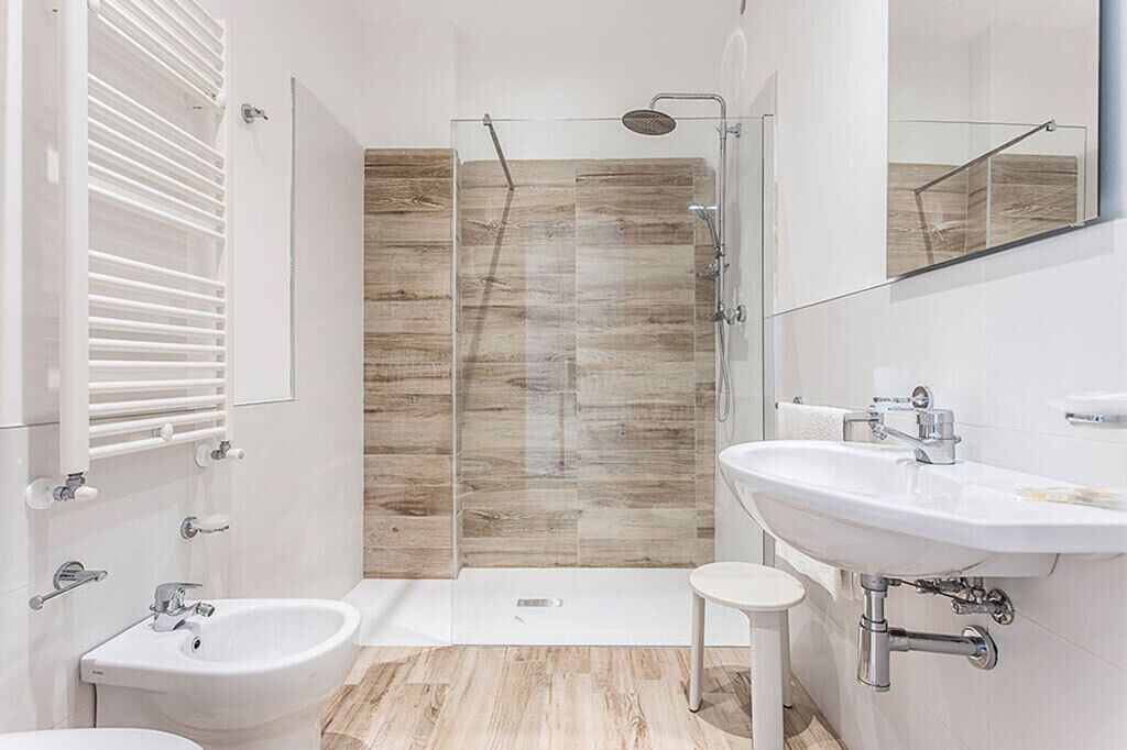 A modern bathroom with a glass shower enclosure, a double sink, and a small stool.