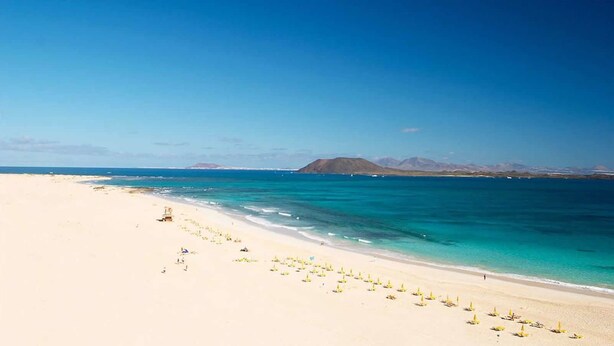 A beach with clear turquoise water, a sandy shore, and a mountain in the background. - GBH Volcanic Beach (La Oliva)
