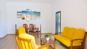 A living room with a yellow sofa, wooden chairs, a dining table, and a potted plant. - GBH Volcanic Beach (La Oliva)