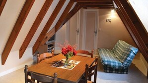 Ein gemütliches Dachzimmer mit Holztisch, Stühlen und einem karierten Sofa.