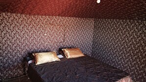 A room with a patterned wall, a bed with a dark quilt, and two pillows.