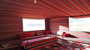 A room with a patterned red and black striped ceiling and walls, a bench with red cushions, and a view of a desert landscape through a window.