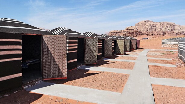 A row of caravan-style tents with a patterned exterior, set against a desert backdrop with rocky formations.