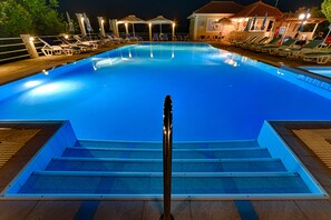 A swimming pool with lounge chairs and umbrellas, surrounded by a wooden deck and a building with a tiled roof. - Ionis Hotel (Kefalonia)