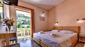 Habitación de hotel con una cama grande, un escritorio con silla, un florero con flores y vistas a una colina.