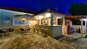 Zona de bar al aire libre con suelo de piedra, mesas y sillas.