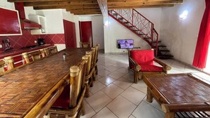 Une pièce spacieuse avec une grande table à manger en bois, une chaise rembourrée de couleur rouge, un téléviseur et un escalier avec une rampe rouge.
