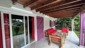 Une terrasse couverte avec un plafond en bois, une porte vitrée donnant sur l’extérieur et deux fauteuils en osier avec des coussins rouges.