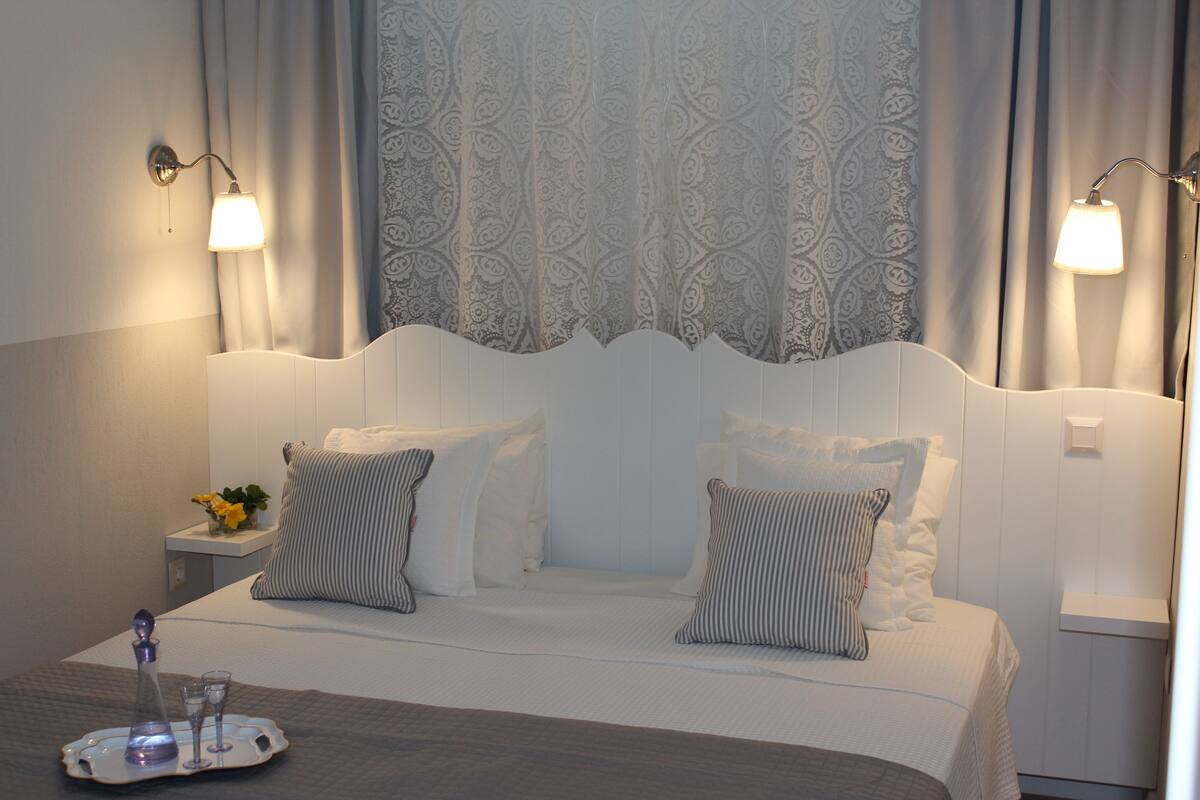 A neatly made bed with two pillows, a bedside table with a vase of flowers, and a tray with a glass and a bottle.