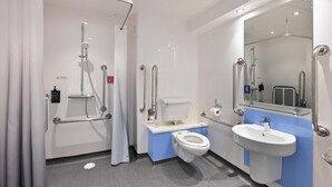 A modern bathroom with a shower, toilet, and sink, equipped with handrails and a glass shower enclosure. - TRAVELODGE WALSALL (WALSALL)