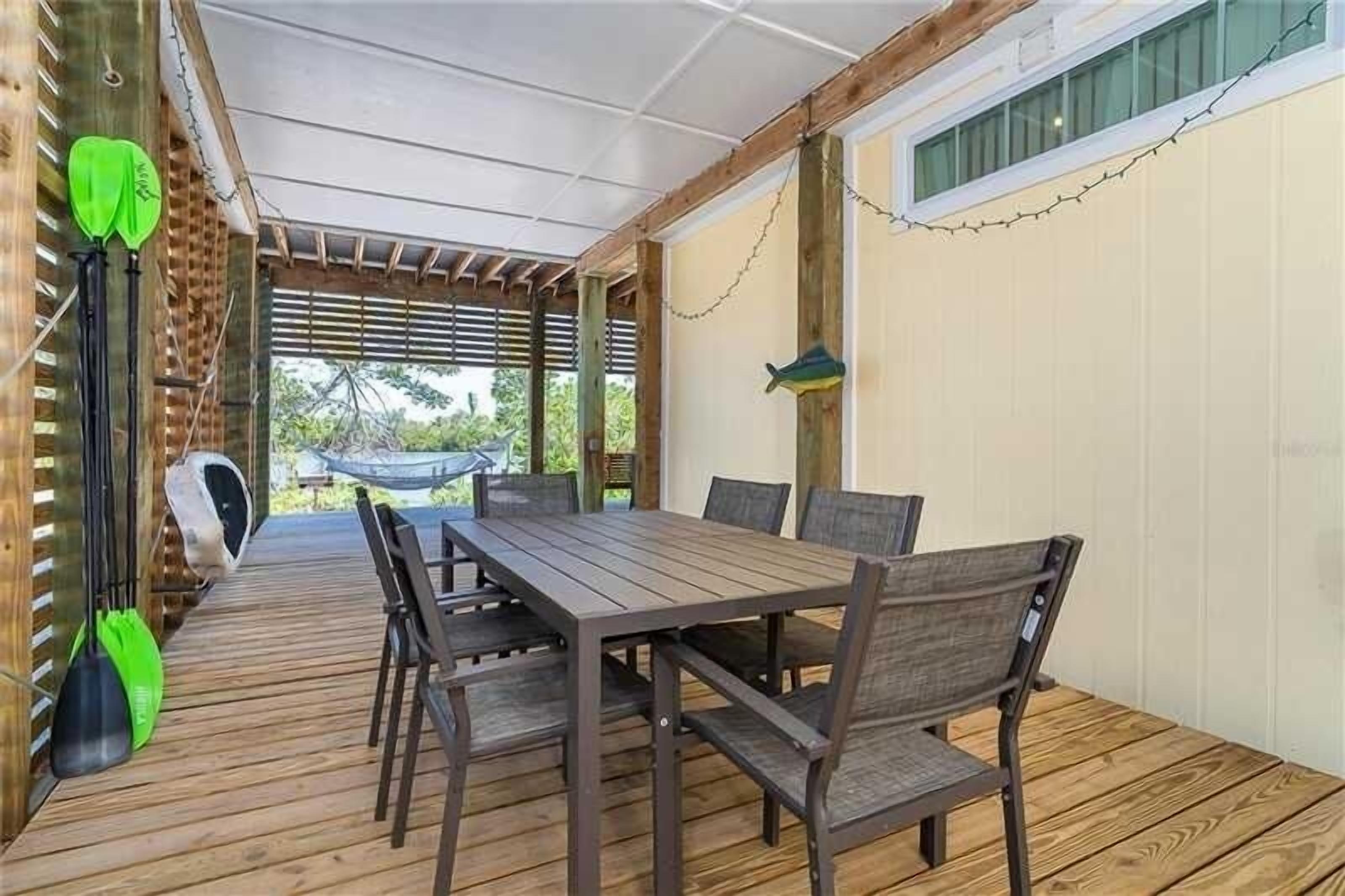 Une terrasse extérieure avec une table et des chaises en bois, un hamac et une décoration en forme de poisson suspendue.