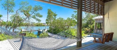 A wooden deck with a hammock and a swing chair overlooking a pool and lush greenery.