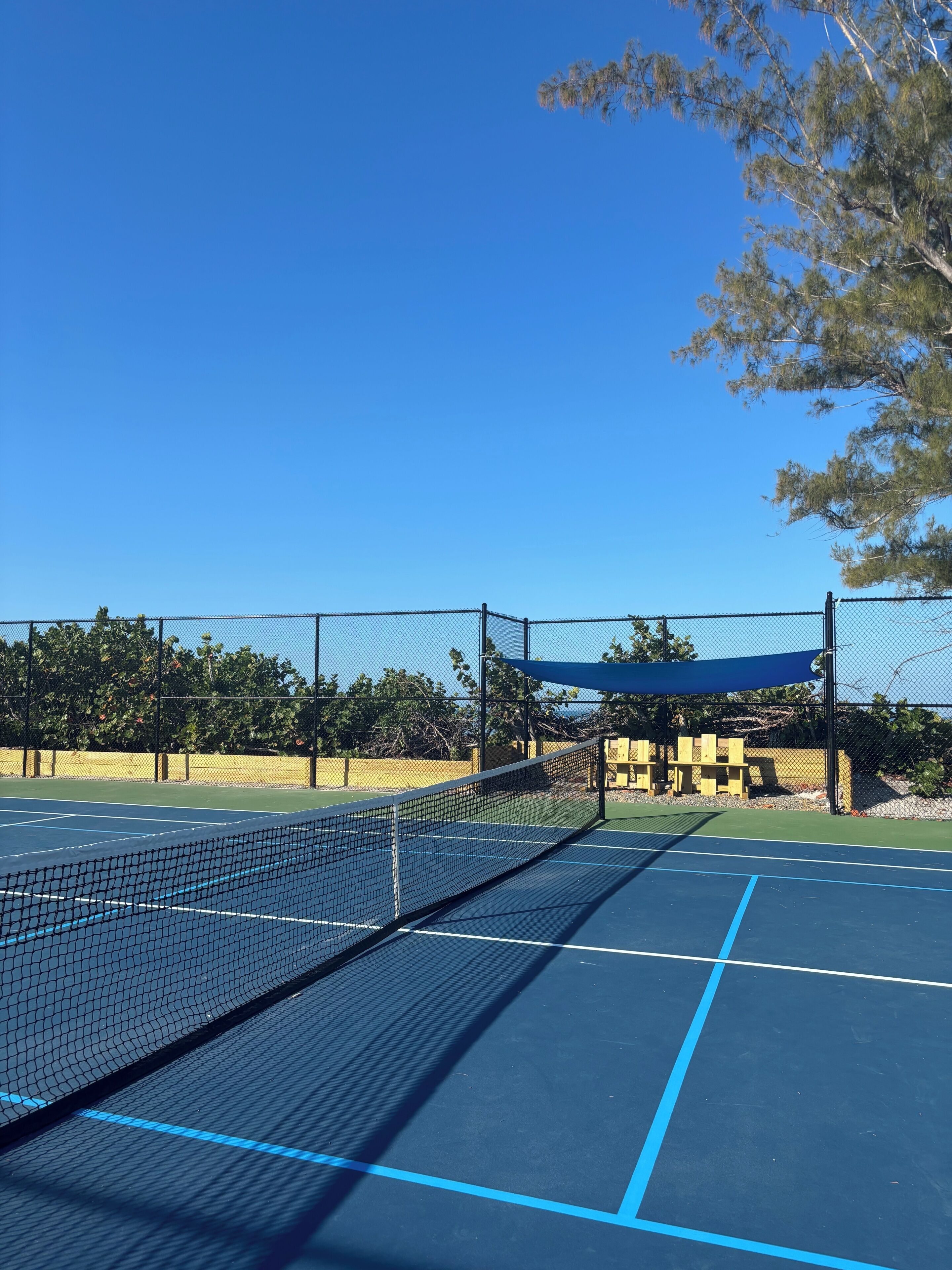 A tennis court with a net, blue lines, and a fence.