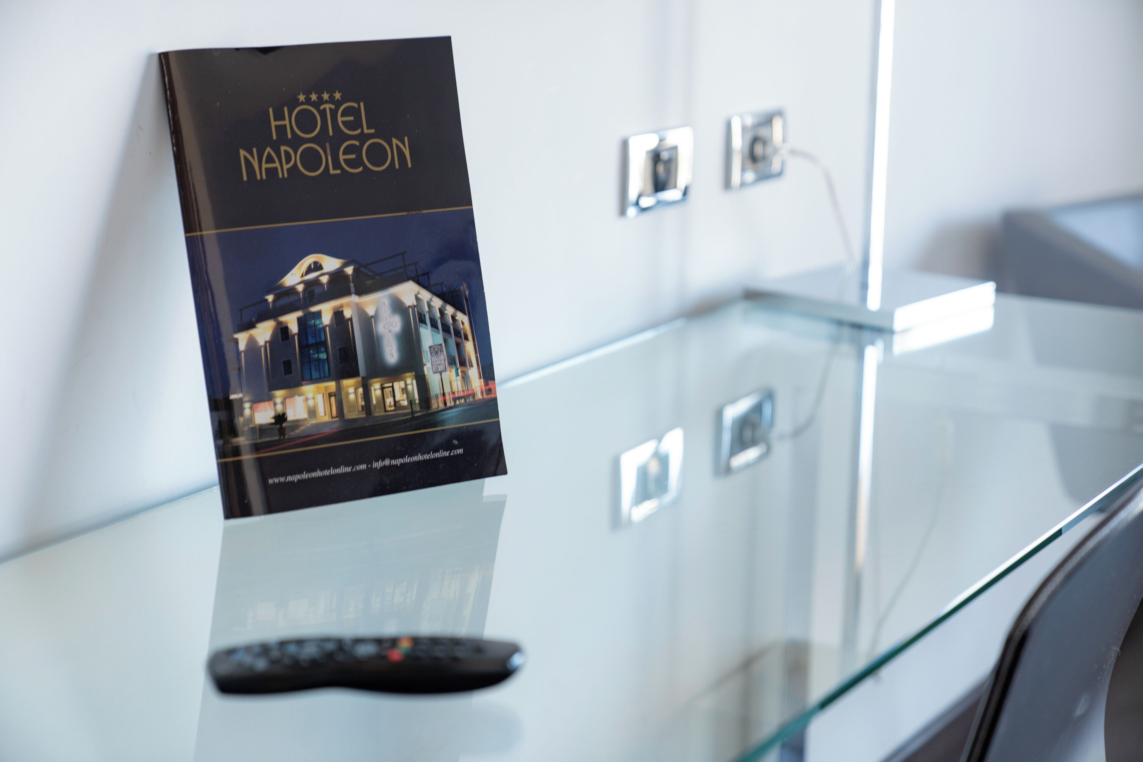 A hotel brochure titled "HOTEL NAPOLEON" on a glass table with a remote control.