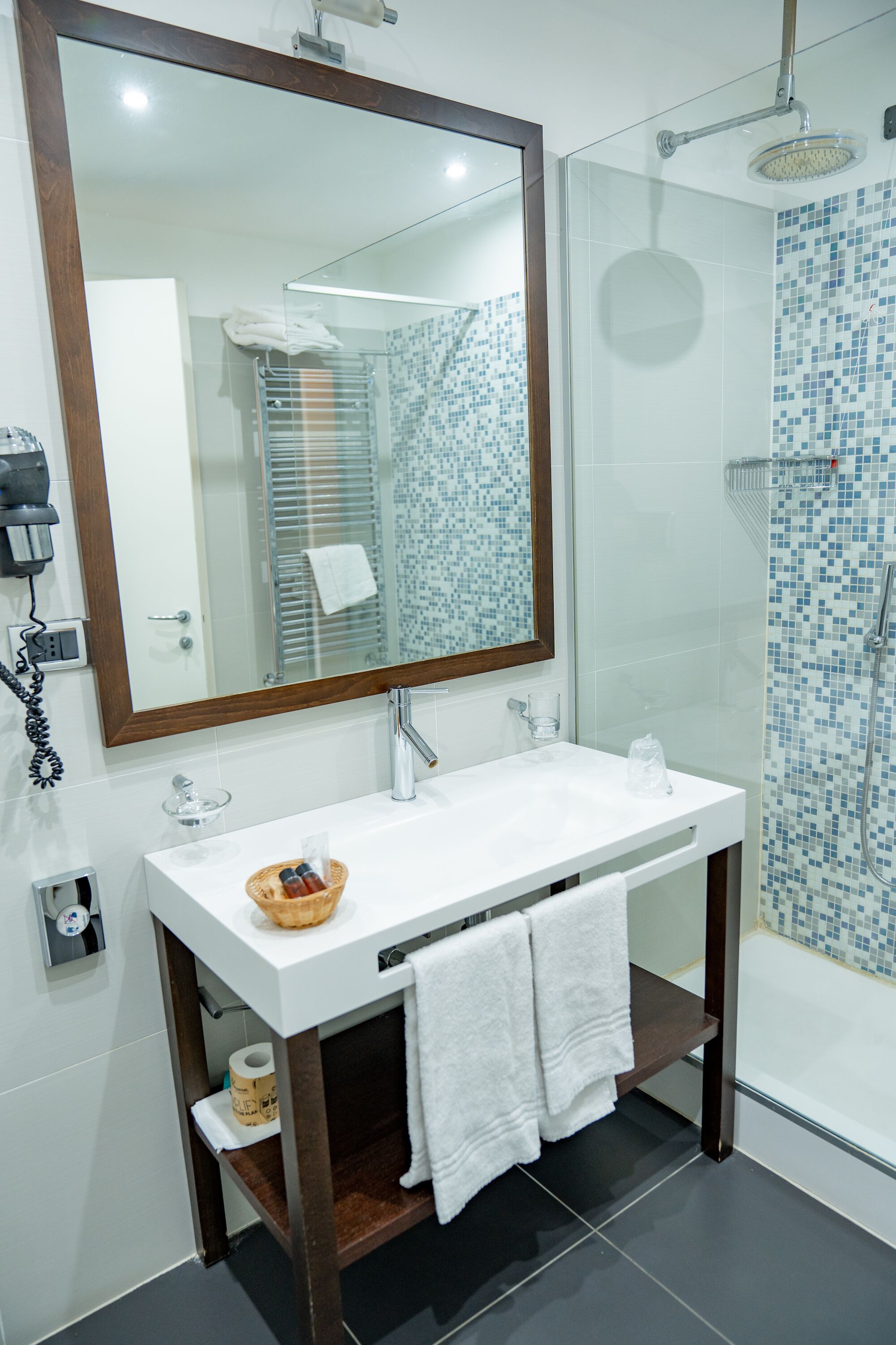 Un baño moderno con un lavamanos blanco, un espejo grande y una ducha con cerramiento de vidrio.