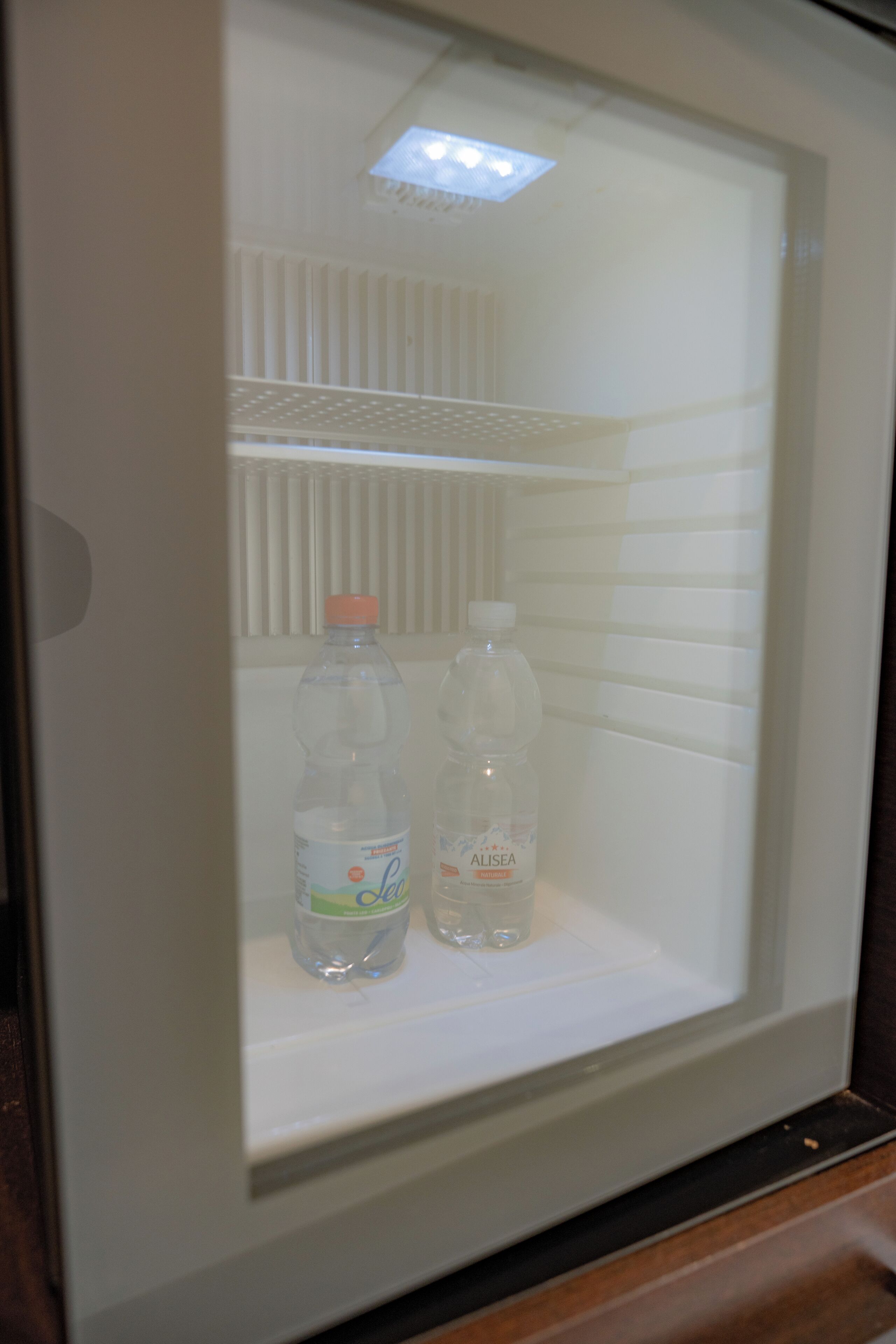 A refrigerator with two bottles of water and a glass.