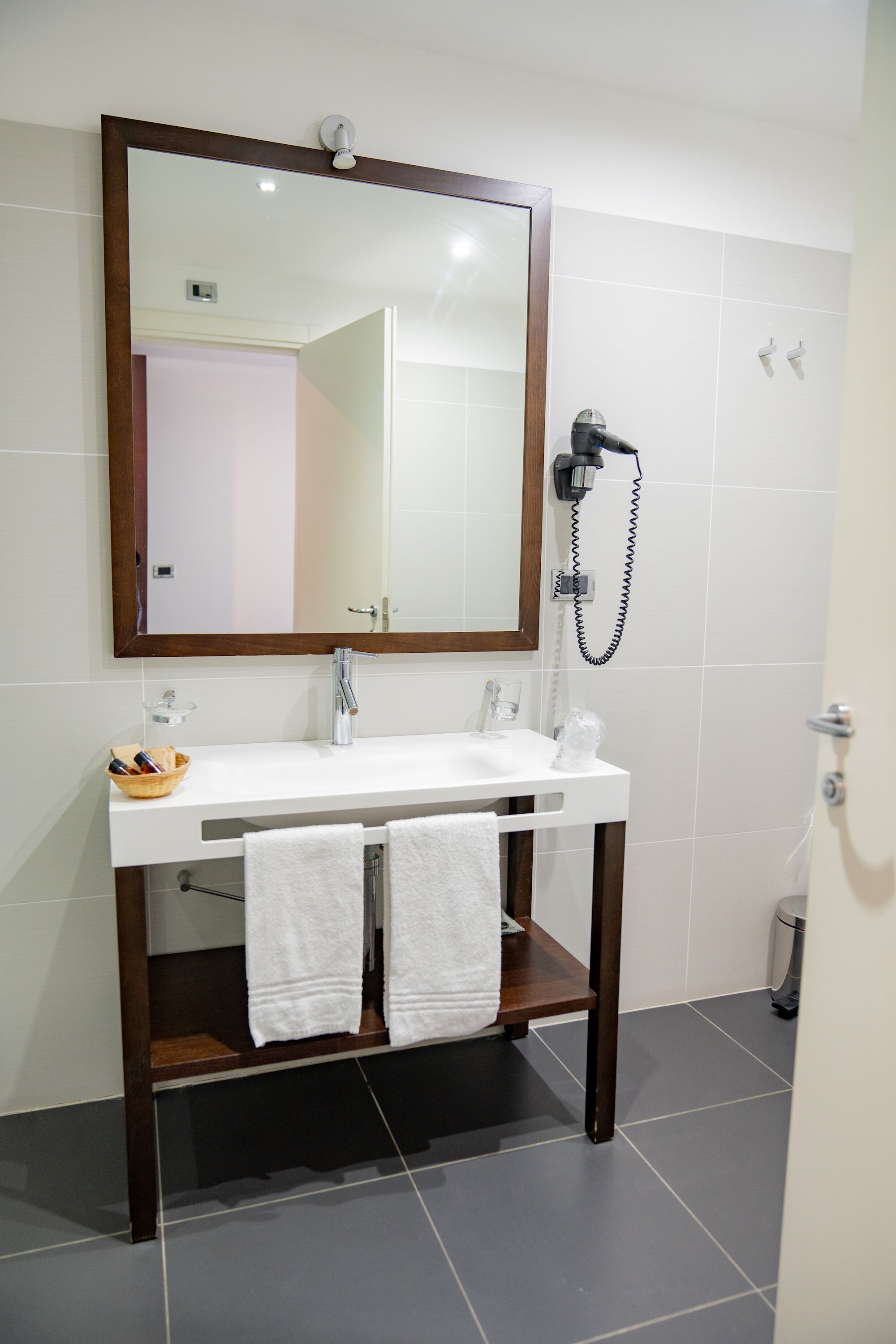 Une salle de bain avec un lavabo blanc, un grand miroir et un sèche-cheveux fixé au mur.