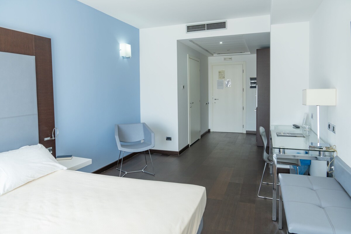 A hotel room with a bed, a desk, a chair, and a bathroom visible through an open door.
