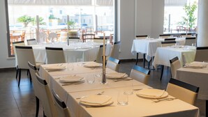 A restaurant with multiple tables set for dining, featuring white tablecloths and chairs, with a view of the city through large windows. - Hotel Napoleon (Melissa)