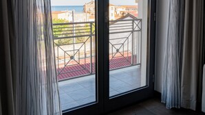 A room with a large sliding glass door leading to a balcony with a view of buildings and a body of water. - Hotel Napoleon (Melissa)