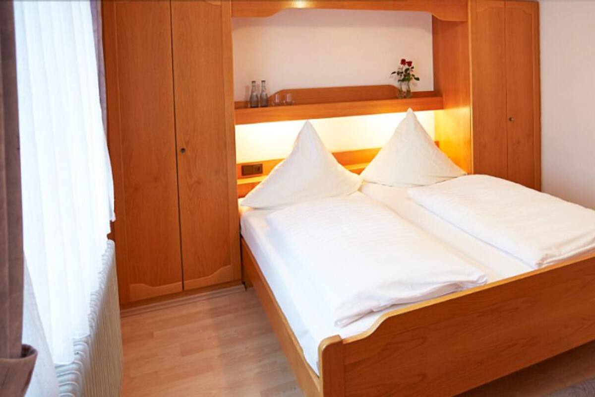 Una cama de madera con sábanas blancas en una habitación con paredes de madera y una estantería sobre la cama.
