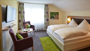 Une chambre d’hôtel avec un lit, une télévision, une chaise, une petite table et un tapis vert.