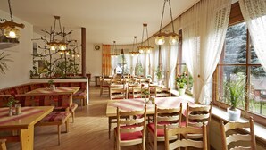 Un restaurant avec des tables et des chaises en bois, des plantes en pot et des luminaires suspendus.