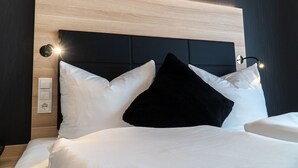 A neatly made bed with white and black pillows, a wooden headboard, and a wall socket. - Hotel Schlafplatz (Rodgau)