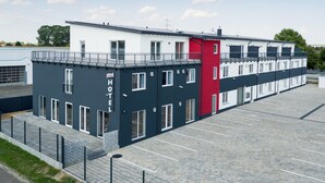 A modern hotel with a flat roof, a red accent wall, and a parking lot. - Hotel Schlafplatz (Rodgau)
