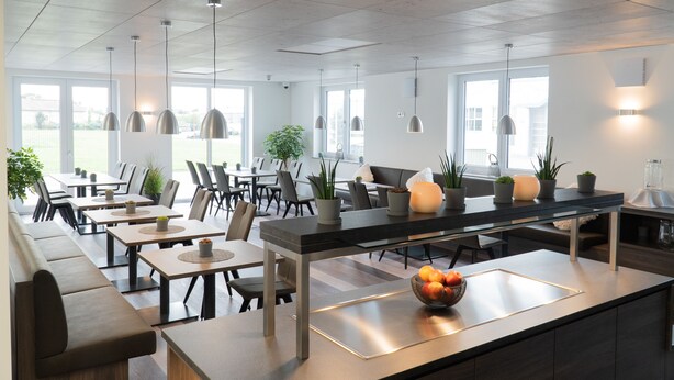 A modern dining area with long communal tables, cushioned seating, and pendant lighting. - Hotel Schlafplatz (Rodgau)