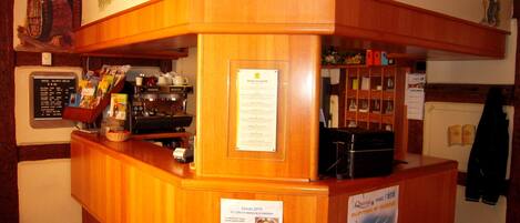 Un mostrador de recepción de madera con una máquina de café, un panel con la carta y un cartel anunciando la temporada 2010.