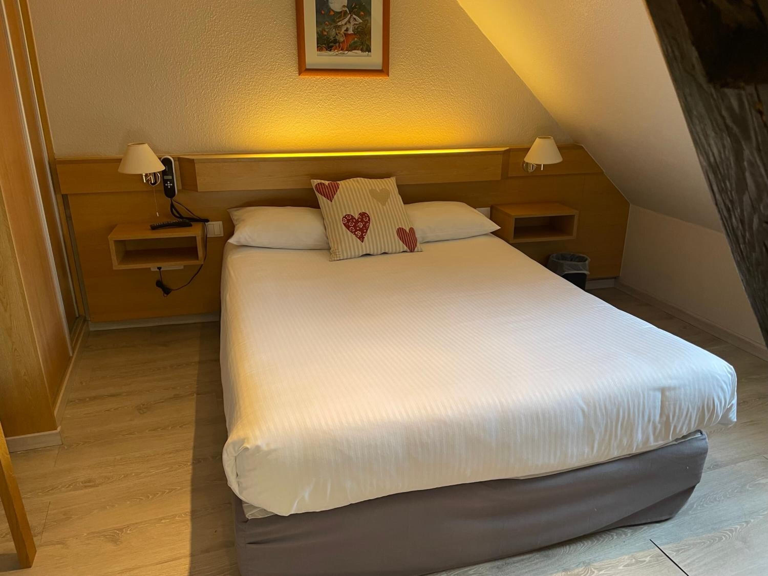 A neatly arranged bedroom with a large bed, two bedside tables with lamps, a small shelf, and a framed picture on the wall.