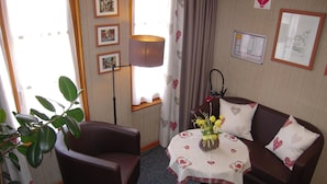 A cozy room with a brown leather sofa, a small round table with a floral tablecloth, and a potted plant. - Hôtel Sainte Odile (Obernai)